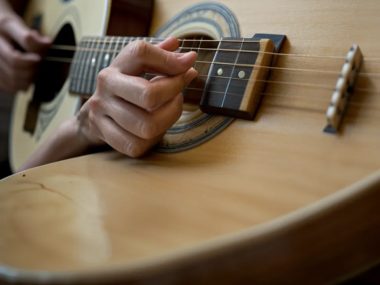 Guitarra acústica junto a una lección del curso Guitarra Master en una tablet, rutina de principiante adulto